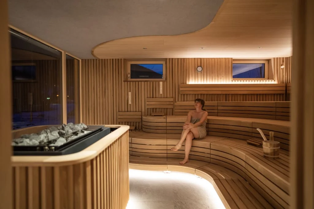 Wooden sauna with benches, sauna stones and a seated woman