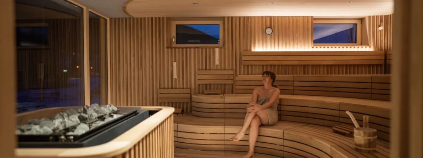 Wooden sauna with benches, sauna stones and a seated woman
