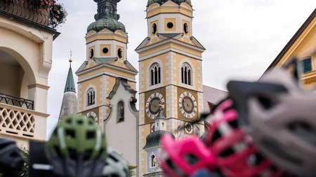 Das war die bike festa Südtirol in Brixen © Brixen Tourismus - Brixen Dom bike festa Südtirol 2026 Kirche mit zwei Uhrturmspitzen, im Vordergrund unscharfe Fahrräder und Helme