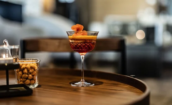 Winterurlaubswoche Roter Cocktail mit orangefarbener Garnitur auf einem Holztisch, daneben ein Glas mit Nüssen