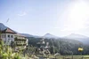 Hotel Maria mit Balkonblumen vor bewaldeten Bergen im Sonnenschein