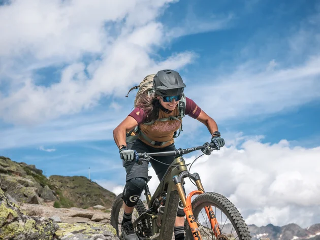 Frau fährt Mountainbike auf felsigem Bergweg bei klarem Himmel