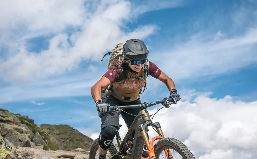 Woman mountain biking on rocky trail under clear blue sky