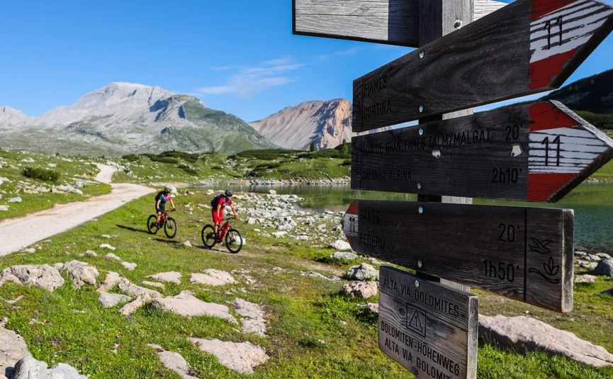 Two cyclists on mountain trail near signpost in the Dolomites