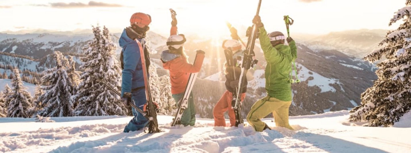 Vier Skifahrer feiern auf schneebedecktem Berg bei Sonnenuntergang