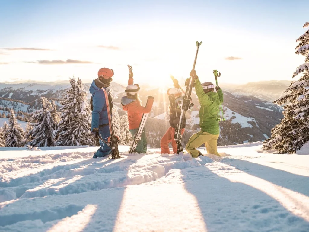 Vier skiërs vieren op besneeuwde berg bij zonsondergang