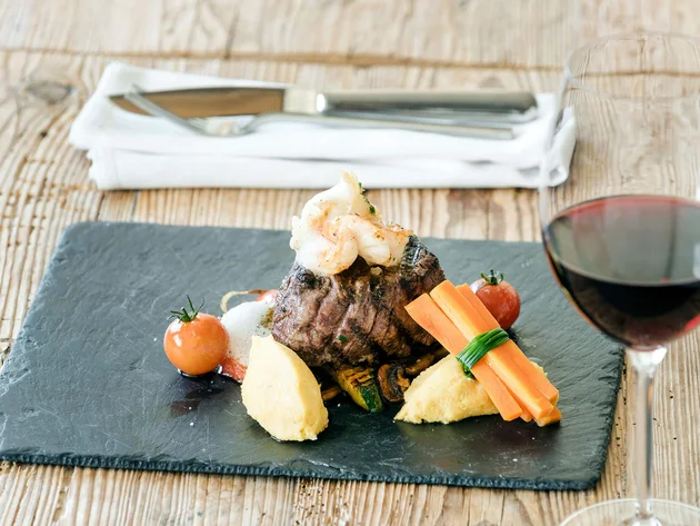 Gourmetgerecht met biefstuk, groenten, aardappelpuree en rode wijn op houten tafel