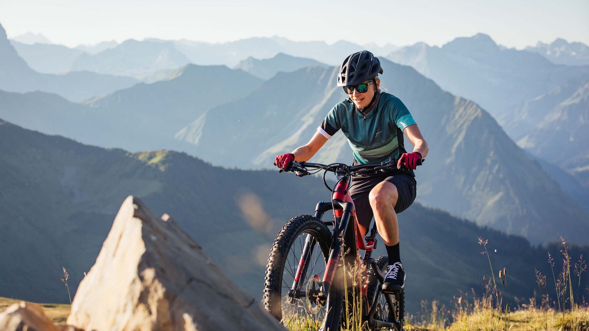 Mountainbike Urlaub für Anfänger
© Bregenzerwald Tourismus - Sebastian Stiphout Frau mountainbiket im Gebirge bei sonnigem Wetter mit Helm und Sonnenbrille