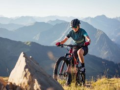 Woman mountain biking in the mountains on a sunny day wearing helmet and sunglasses