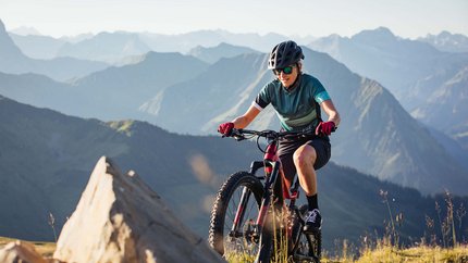 Frau mountainbiket im Gebirge bei sonnigem Wetter mit Helm und Sonnenbrille