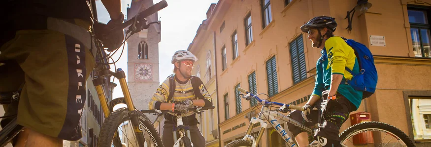 Drei Radfahrer mit Mountainbikes stehen in der Sonne auf gepflastertem Platz