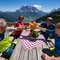 Vier Personen stoßen mit Getränken auf Bergterrasse mit Alpenpanorama an