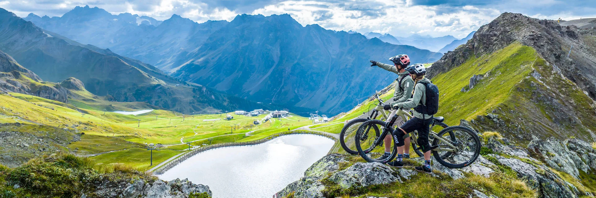 Zwei Mountainbiker auf Felsen mit Blick auf See und Berge