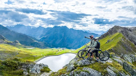 Zwei Mountainbiker auf Felsen mit Blick auf See und Berge
