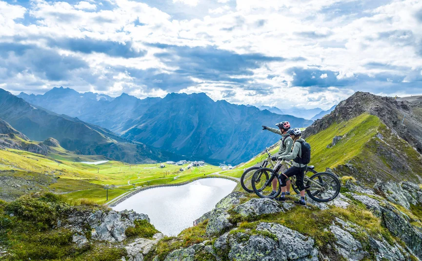 Two mountain bikers on rocks overlooking lake and mountains