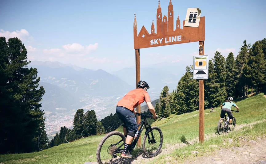 Zwei Mountainbiker fahren auf einem Bergweg unter einem Schild mit Aufschrift Sky Line