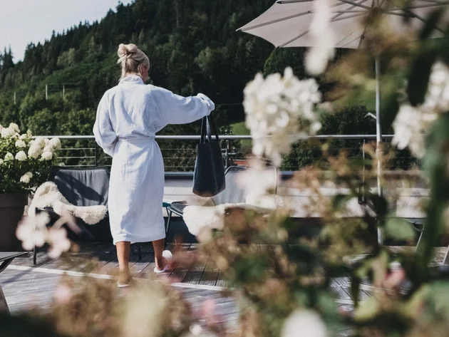 Was steckt hinter dem Umweltengagement von Bikehotels? © Biohotel Rupertus Frau im Bademantel auf Terrasse mit Blumen und Bergen im Hintergrund