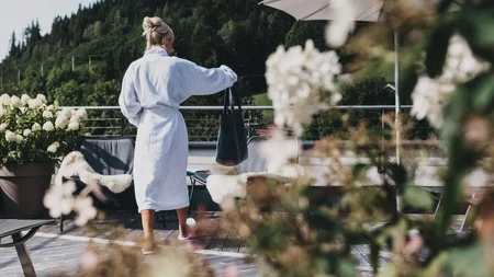 Was steckt hinter dem Umweltengagement von Bikehotels? © Biohotel Rupertus Frau im Bademantel auf Terrasse mit Blumen und Bergen im Hintergrund