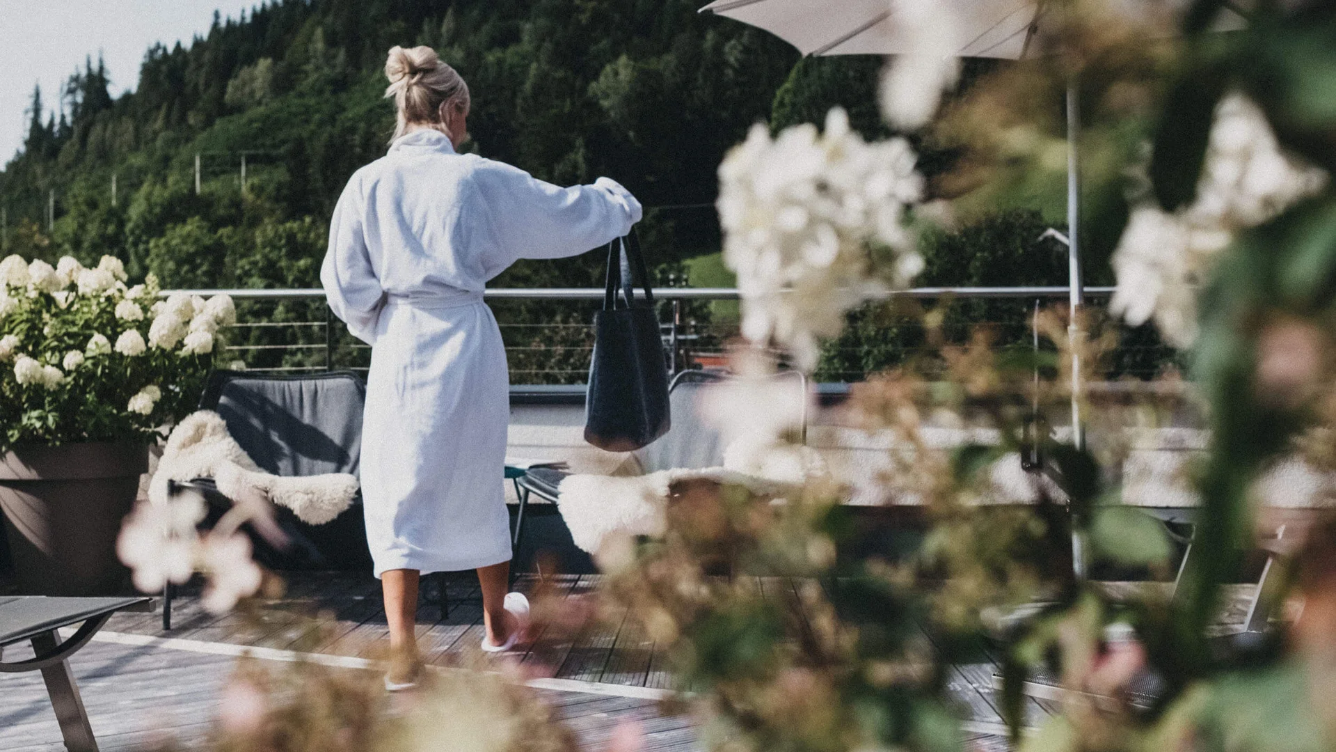 Good to know: 9 Wellness-Funfacts © Biohotel Rupertus Frau im Bademantel auf Terrasse mit Blumen und Bergen im Hintergrund