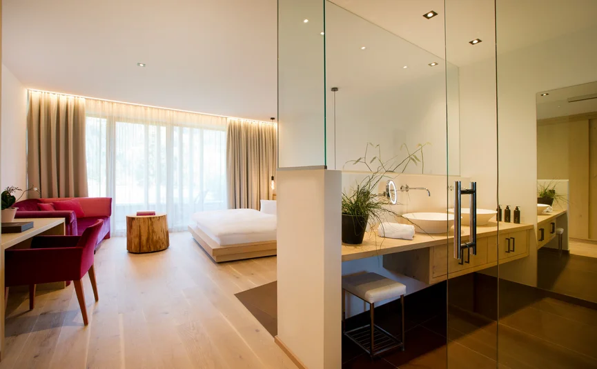 Modernes Hotelzimmer mit Glasbad, Holzboden und rotem Sofa