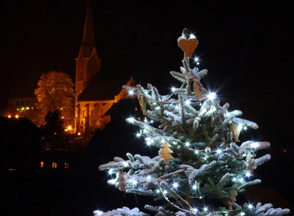 Weihnachtsbaum mit Lichterkette und Schnee bei Nacht vor einer Kirche
