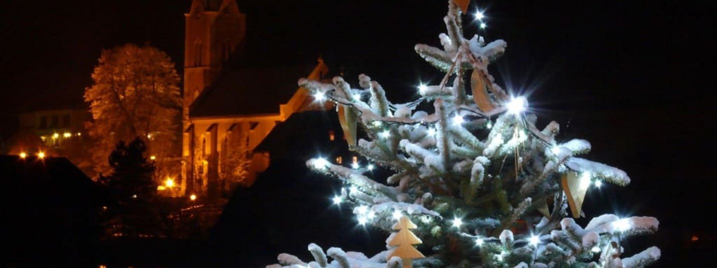 Weihnachtsbaum mit Lichterkette und Schnee bei Nacht vor einer Kirche