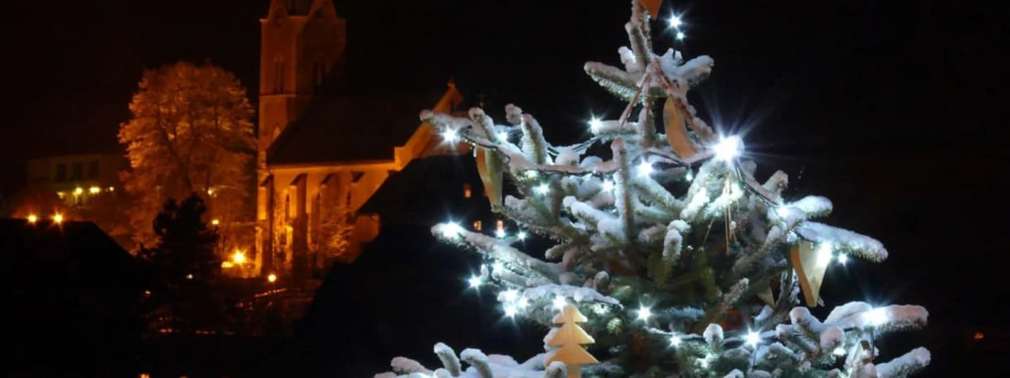 Weihnachtsbaum mit Lichterkette und Schnee bei Nacht vor einer Kirche