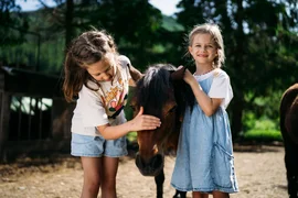 Twee meisjes aaien een pony buiten op een boerderij