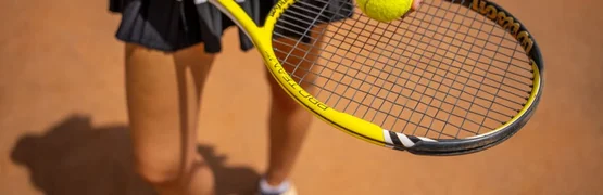 Frau hält einen Tennisball und Tennisschläger auf Sandplatz