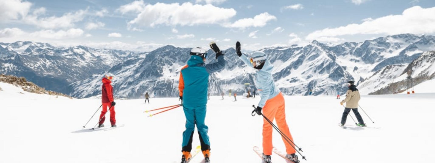 Two skiers highfiving on snowy slope with mountain background