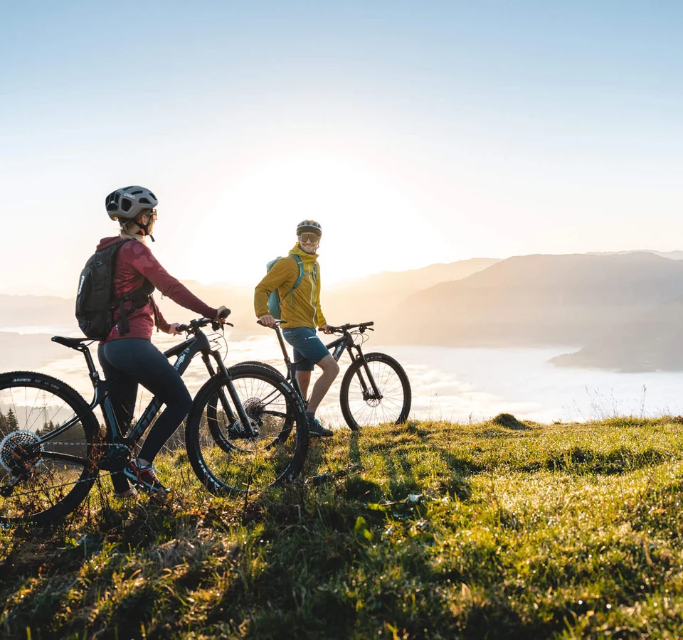 Zwei Radfahrer auf einem Berg mit Blick auf Sonnenaufgang und nebliges Tal