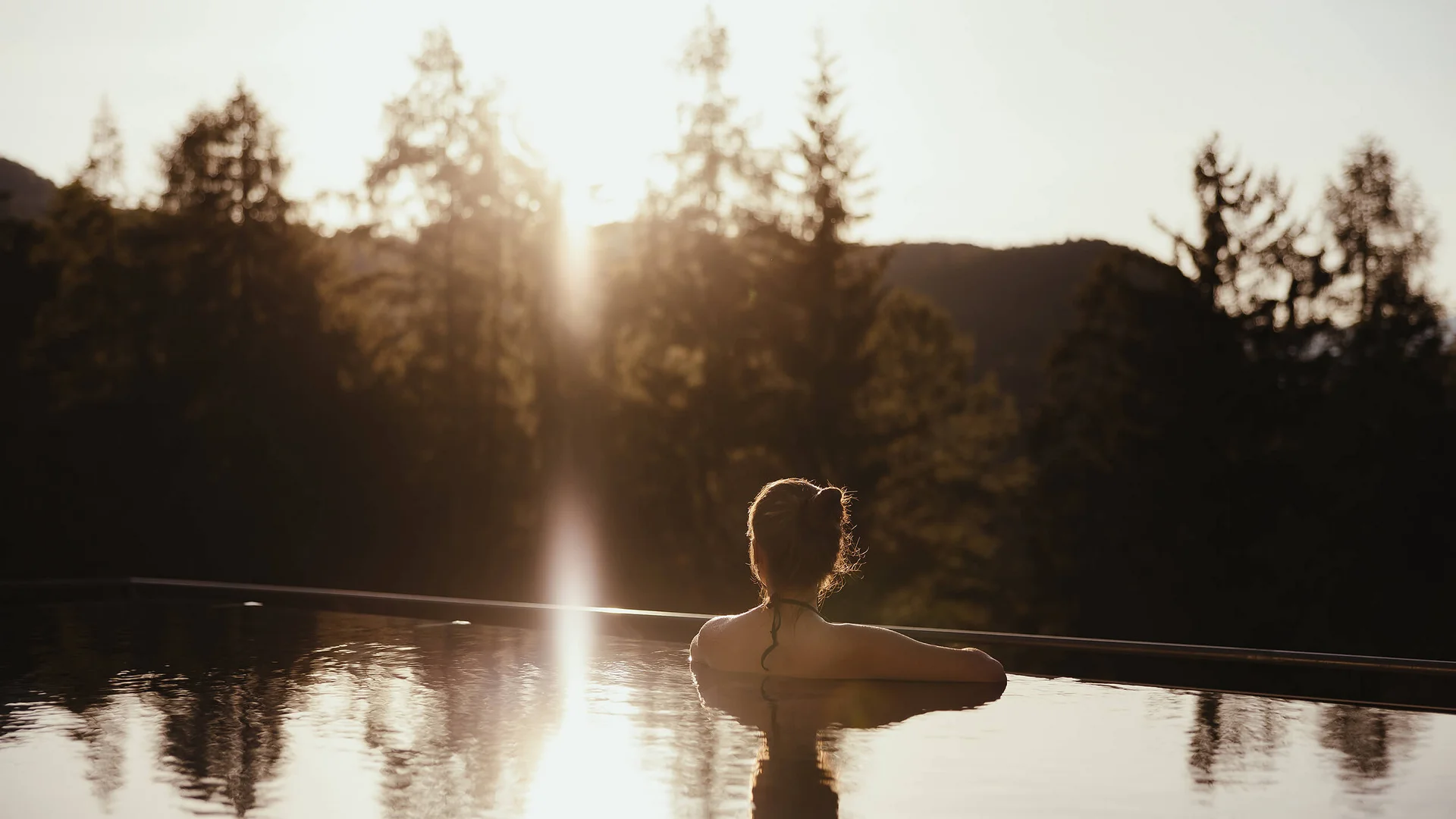 Good to know: 9 Wellness-Funfacts © Alex Moling Frau entspannt im Pool mit Blick auf sonnenbeschienene Bäume und Berge