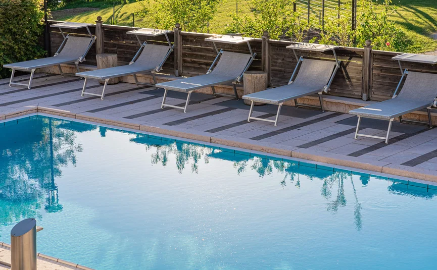Empty lounge chairs beside a clear blue swimming pool in a garden