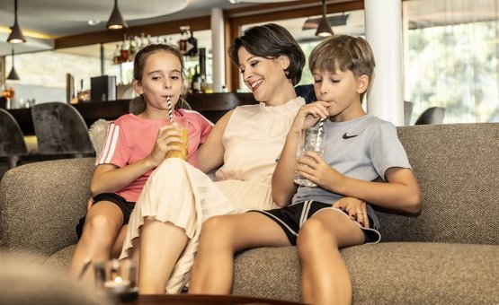 Vrouw met twee kinderen die sap drinken op de bank thuis