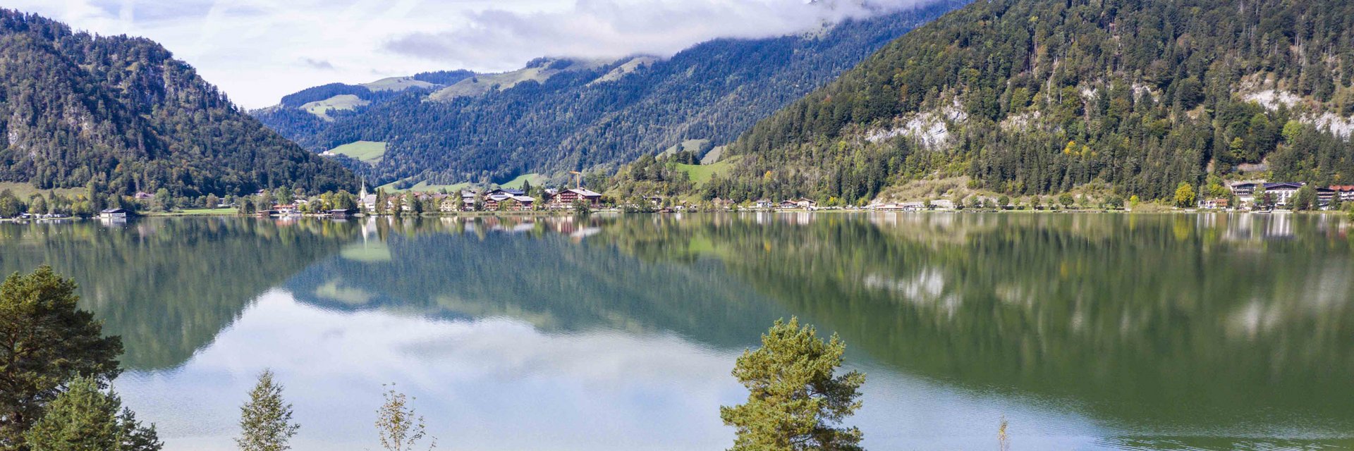 Bergmeer met weerspiegeling van bossen en bergen onder een bewolkte lucht