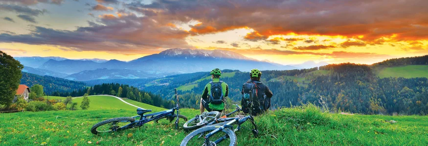 Zwei Radfahrer sitzen auf einer Wiese und schauen in die Bergsonne.
