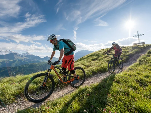 Zwei Mountainbiker fahren auf einem Bergpfad bei Sonnenschein