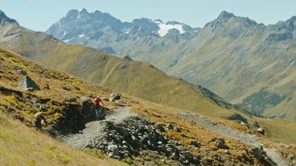 Mountainbiker auf Schotterweg in den Alpen mit schneebedeckten Bergen im Hintergrund