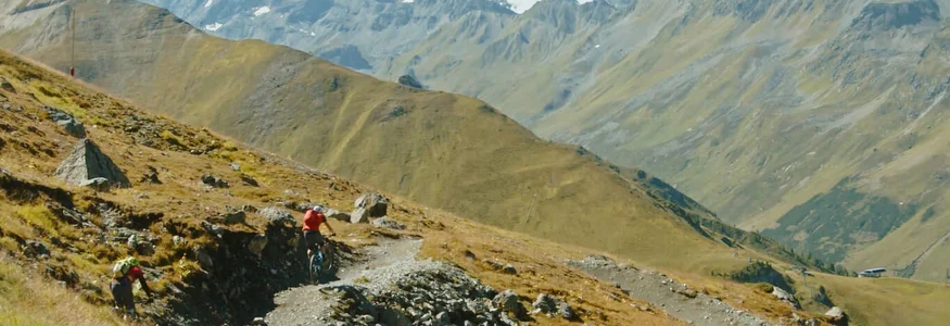 Mountainbiker auf Schotterweg in den Alpen mit schneebedeckten Bergen im Hintergrund
