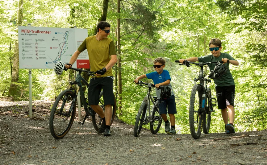 Vater und zwei Kinder schieben Mountainbikes auf Waldweg am MTB-Trailcenter