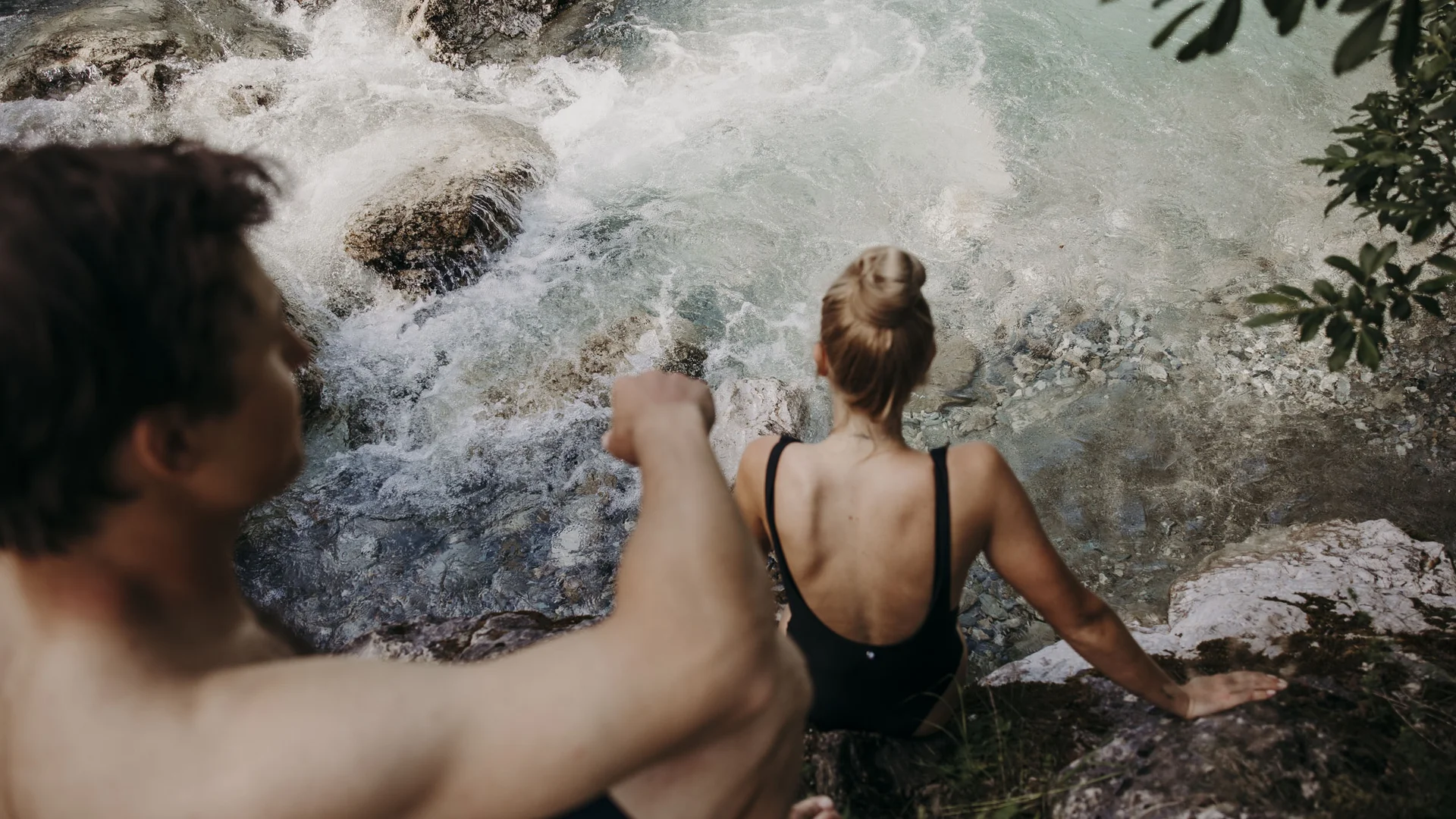 Personen in Badebekleidung klettern auf Felsen am Flussufer