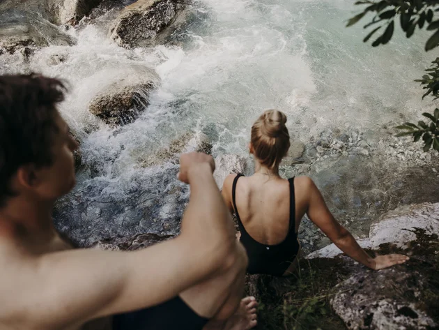 Was steckt hinter dem Umweltengagement von Bikehotels? Personen in Badebekleidung klettern auf Felsen am Flussufer