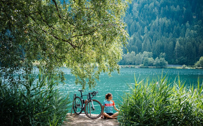 Bike Boutique Hotel Lindenhof **** © Martin Hofmann Frau entspannt mit Fahrrad an einem See in bewaldeter Landschaft
