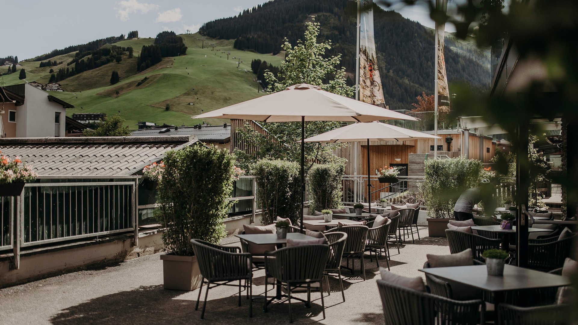 Außenterrasse mit Tischen, Stühlen und Sonnenschirmen vor grünen Bergen