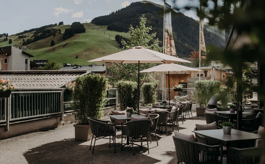 Outdoor terrace with tables, chairs, umbrellas and green mountains in background