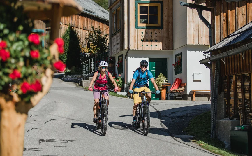 Two cyclists riding through a village with wooden houses in sunny weather