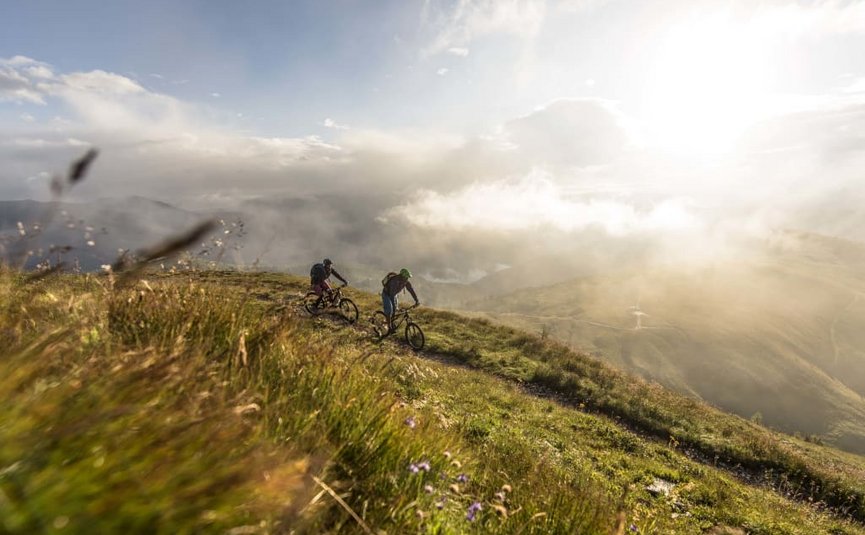 Zwei Mountainbiker fahren auf einem Bergpfad bei sonnigem Wetter und Nebel