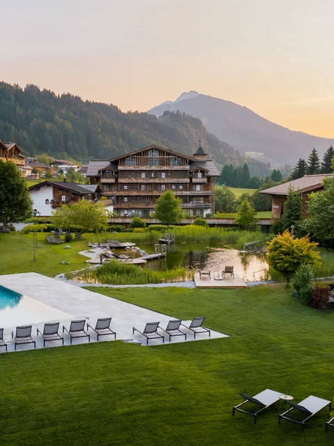 Bergresort mit Pool, Liegestühlen und grüner Landschaft im Sonnenuntergang