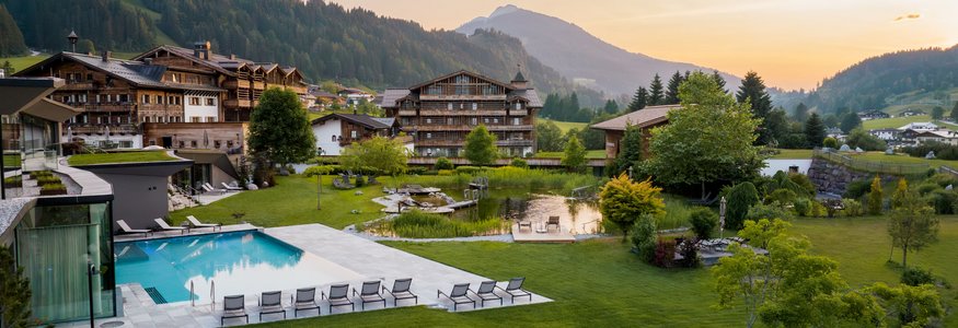 Bergresort mit Pool, Liegestühlen und grüner Landschaft im Sonnenuntergang
