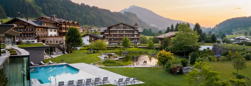 Bergresort mit Pool, Liegestühlen und grüner Landschaft im Sonnenuntergang
